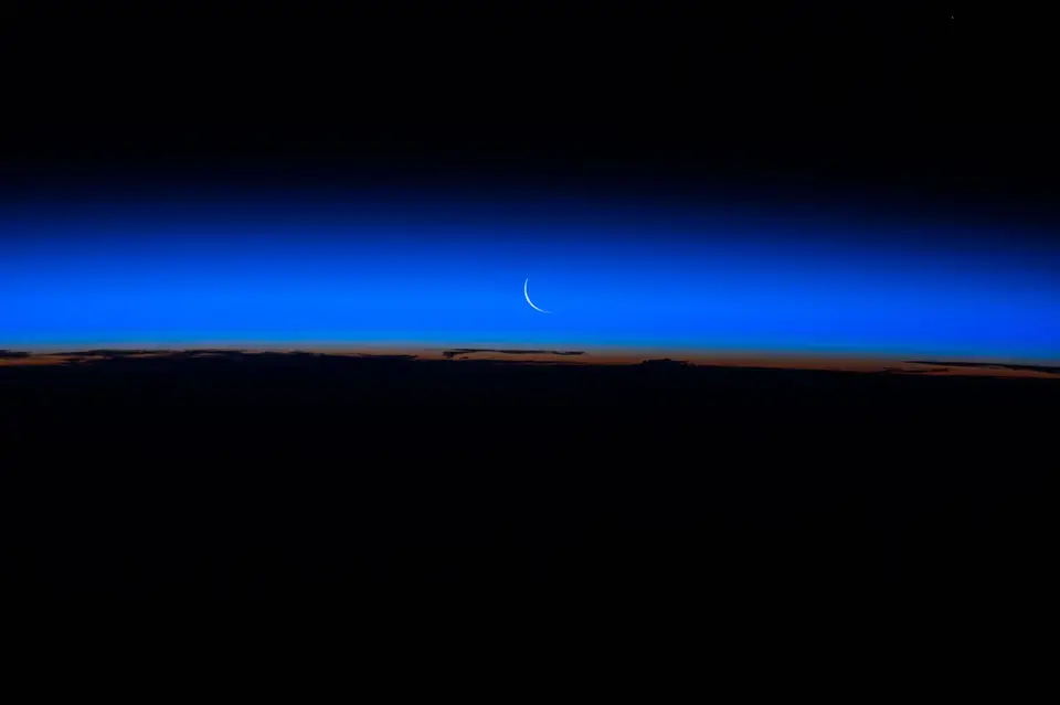 A thin crescent Moon above Earth's glowing edge, seen from space.