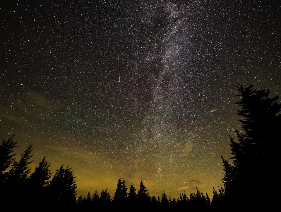 A meteor streak in a starry sky over a dark horizon.
