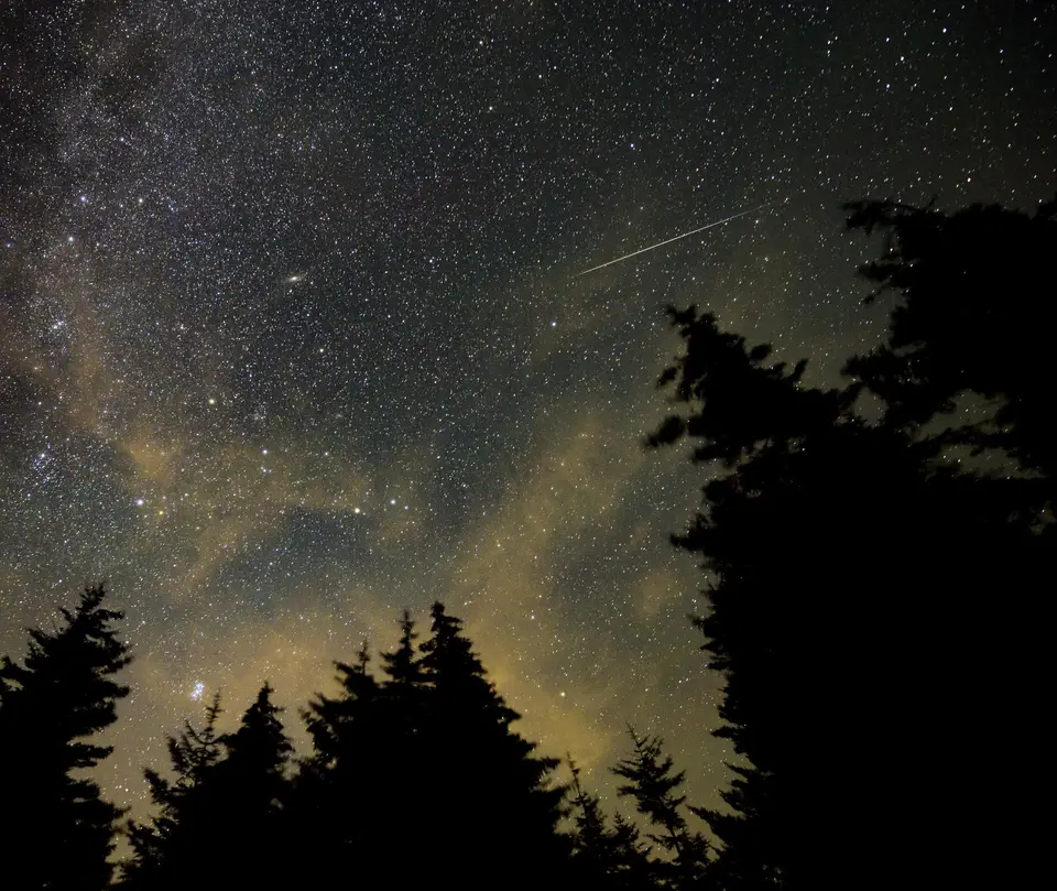 A meteor streak among the stars above a dark ridge.