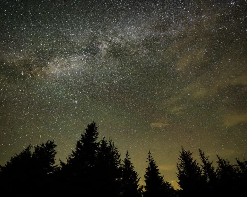A long meteor trail across a sky full of stars.